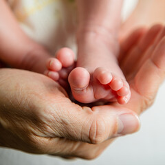 Extreme close-up of a parent's hands gently holding the tiny feet of a newborn baby under soft natural light
