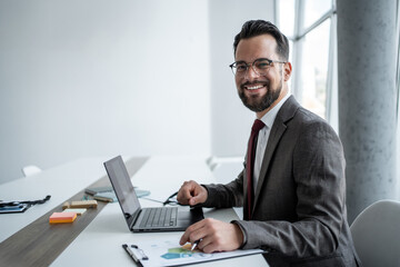 Happy businessman analyzing charts and working on laptop in modern office