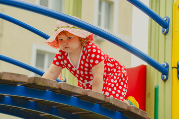 A young child wearing a red polka dot dress and a hat is climbing on colorful playground equipment The sun is shining in a vibrant outdoor park setting creating a joyful atmosphere