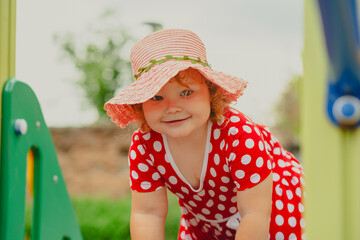 A young child wearing a red polka dot dress and a hat is climbing on colorful playground equipment The sun is shining in a vibrant outdoor park setting creating a joyful atmosphere