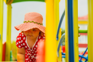 A young child wearing a red polka dot dress and a hat is climbing on colorful playground equipment The sun is shining in a vibrant outdoor park setting creating a joyful atmosphere