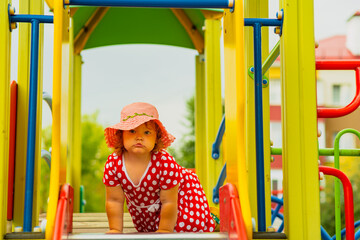 A young child wearing a red polka dot dress and a hat is climbing on colorful playground equipment The sun is shining in a vibrant outdoor park setting creating a joyful atmosphere