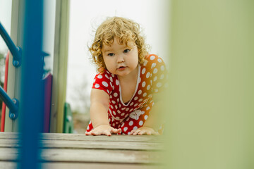 A young child wearing a red polka dot dress and a hat is climbing on colorful playground equipment The sun is shining in a vibrant outdoor park setting creating a joyful atmosphere