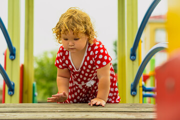 A young child wearing a red polka dot dress and a hat is climbing on colorful playground equipment The sun is shining in a vibrant outdoor park setting creating a joyful atmosphere