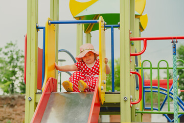 A happy kid in a red polka dot dress is sliding down a playground slide Bright colors surround her and the atmosphere is joyful during a sunny day with playful clouds