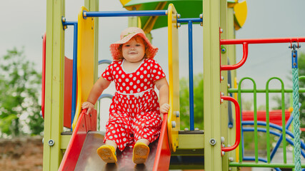 A happy kid in a red polka dot dress is sliding down a playground slide Bright colors surround her and the atmosphere is joyful during a sunny day with playful clouds