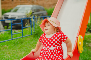 A happy kid in a red polka dot dress is sliding down a playground slide Bright colors surround her and the atmosphere is joyful during a sunny day with playful clouds