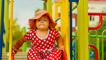 A happy kid in a red polka dot dress is sliding down a playground slide Bright colors surround her and the atmosphere is joyful during a sunny day with playful clouds