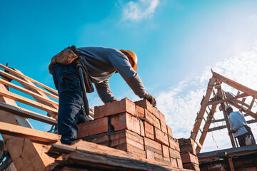 mason laying final brick courses while carpenters prepare roof structure materials