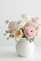 Obraz premium Soft pastel bouquet of ranunculus and roses in blush, white, and cream tones arranged in a simple white ceramic vase