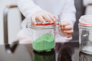 A girl closes a metal latch on a jar of green sugar.