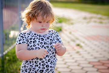 In a sunny park a young child with curly hair focuses on tearing petals from a bright daisy