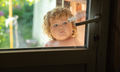 A young child with curly hair examines the screen door showing curiosity and wonder Sunlight filters through illuminating their playful expression on a warm day