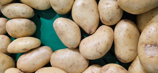 Raw light brown potatoes with smooth, slightly speckled skins rest on a green surface, showing...