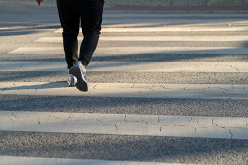 Person is walking on a crosswalk in bright daylight. The pavement displays distinct shadow patterns...