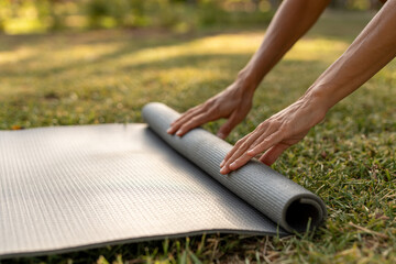 Close-up of hands rolling out a yoga mat on the grass in a sunny outdoor park, preparing for a...