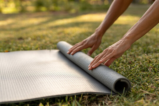 Close-up of hands rolling out a yoga mat on the grass in a sunny outdoor park, preparing for a wellness or fitness session