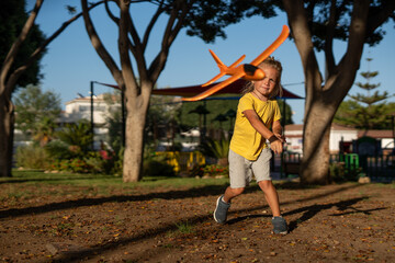 Energetic young boy throwing an orange toy airplane in a park, mid-motion with dynamic expression,...