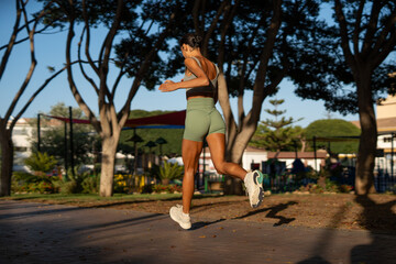 Fit athletic woman doing cardio training outdoors, captured mid-jump with her back to the camera,...