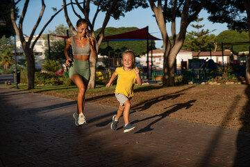 Happy fit mother and her energetic young son running together in the park on a sunny day, bonding...