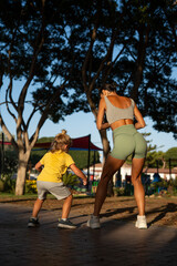 Obraz premium Back view of a fit woman and her young son exercising together in a sunny park, both squatting with energy and focus, enjoying an outdoor workout under the shade of tall trees