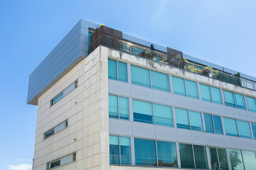 Modern building with sleek lines and blue-tinted windows under a clear sky, featuring a rooftop terrace with greenery, reflecting contemporary urban architecture in Portugal.
