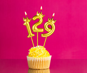 Birthday celebration with number 129 candle - Yellow cupcake on a pink background
