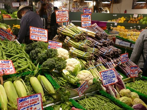 Fresh organic vegetables at Pike Place Market, Seattle, displaying asparagus, broccoli, cauliflower, corn, and peas near browsing customer