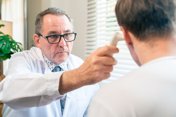 Doctor using ear infrared thermometer measure temperature and examine male patient at clinic. Physician medical healthcare support, disease diagnosis. Health checkup, hospital wellness consultation.