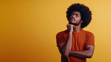 A thoughtful African American man touching his chin in deep contemplation, standing against a yellow studio background.