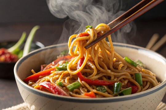 Delicious steaming Asian noodles with colorful vegetables served in a ceramic bowl with chopsticks