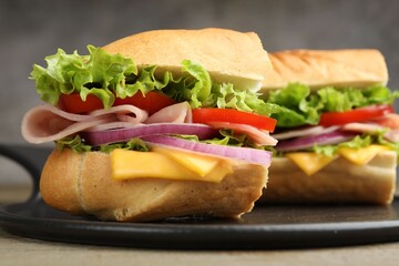 Pieces of tasty baguette sandwich with ham, cheese and vegetables on table against grey background, closeup