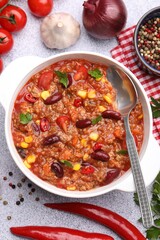 Tasty chili con carne in bowl and ingredients on grey table, flat lay