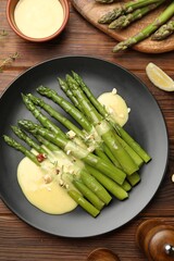 Tasty cooked asparagus served with sauce on wooden table, flat lay