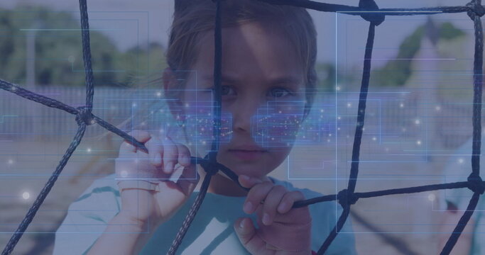 Gripping netting girl wearing turquoise shirt gazing at viewer at playground with digital overlay - Powered by Adobe