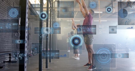 Extending arms overhead man wearing maroon shirt at training gym, with digital HUD overlay