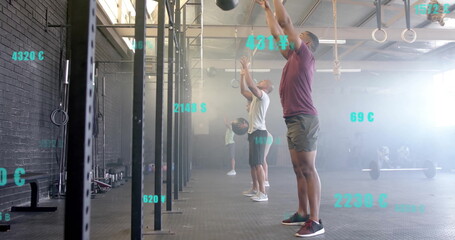 Man wearing maroon shirt and shorts tossing medicine ball overhead in CrossFit gym, with metrics