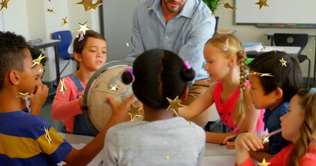 Guiding male teacher and children leaning over globe and pointing at map in classroom, with globe