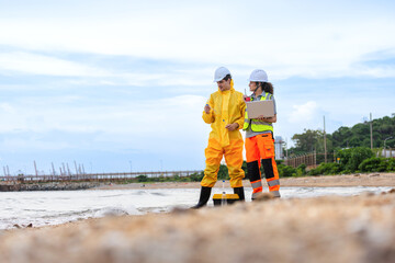 Researchers in Protective Gear Studying Water Quality at Site, Environmental Scientists Collecting Water Samples for Analysis, Ecologists Working on Beach, Monitoring Environmental Contamination