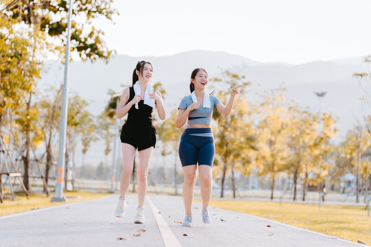 Two young women in exercise clothes are walking together, jogging together in the park.