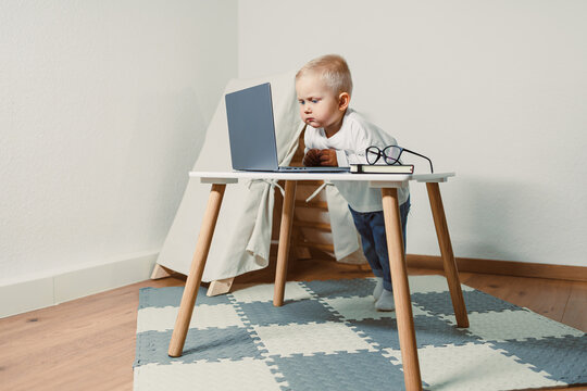 In a cozy workspace, a curious toddler explores a laptop, highlighting the importance of playful learning and early tech exposure for child development during critical formative years