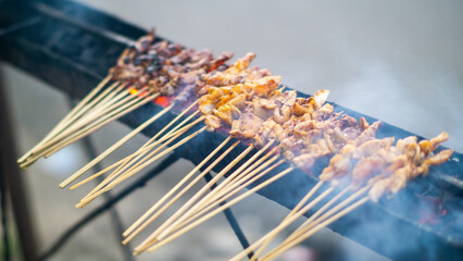 Traditional Indonesian satay skewers being grilled on a charcoal stove with smoke rising.