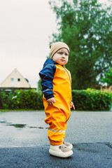 Fototapeta premium A Charming Toddler Dressed in Bright Yellow Rain Gear Stands in Front of a Beautiful Lush Green Background, Creating a Vivid Visual Impression with a Playful and Joyful Atmosphere