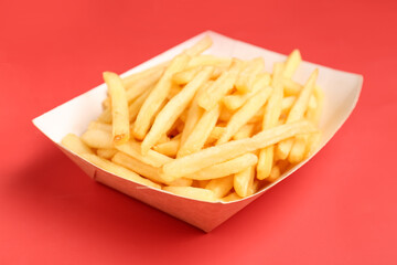Paper box with tasty french fries on red background