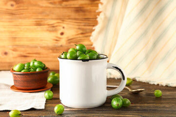 Cup and bowl with fresh gooseberries on wooden background