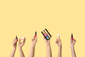 Female hands with eyeshadows palette, foundation and lipsticks on yellow background
