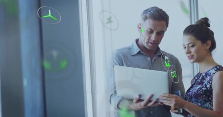 Man holding laptop while woman tapping trackpad and animating green energy icons for analysis - Powered by Adobe