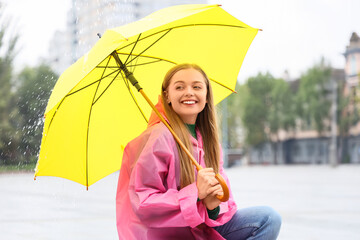 Beautiful young happy woman in raincoat with umbrella sitting on rainy day outdoors