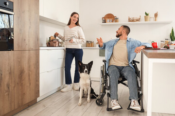 Young man in wheelchair, with wife and dog cooking in kitchen