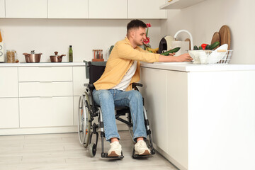 Young man in wheelchair washing vegetables at home